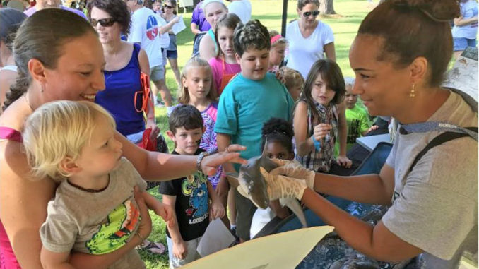 A volunteer instructor sharing information with families about sharks and other fish species at an outdoor event.