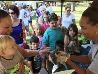 A volunteer instructor sharing information with families about sharks and other fish species at an outdoor event.