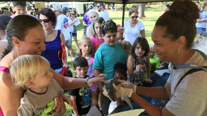 A volunteer instructor sharing information with families about sharks and other fish species at an outdoor event.